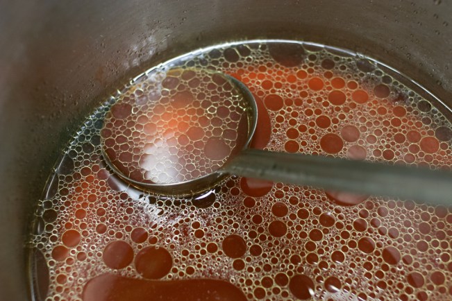 Close up shop of a pot of rich meat stock with a ladle